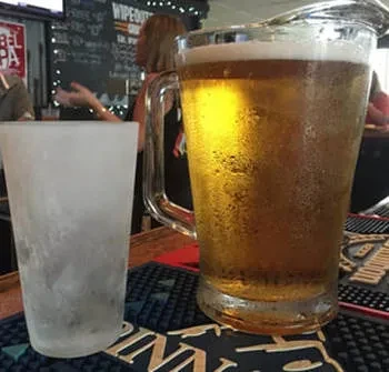 Condensing golden beer pitcher with a frosted glass on a bar mat.