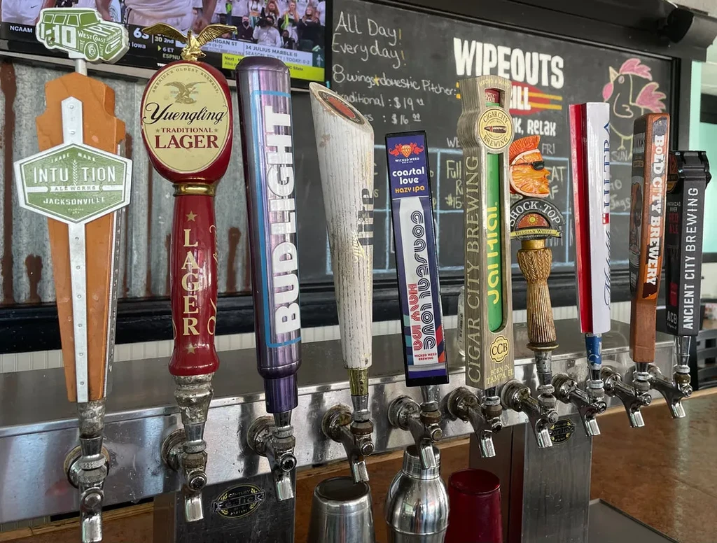Close-up of diverse beer tap handles on a bar, with a menu chalkboard and TV.