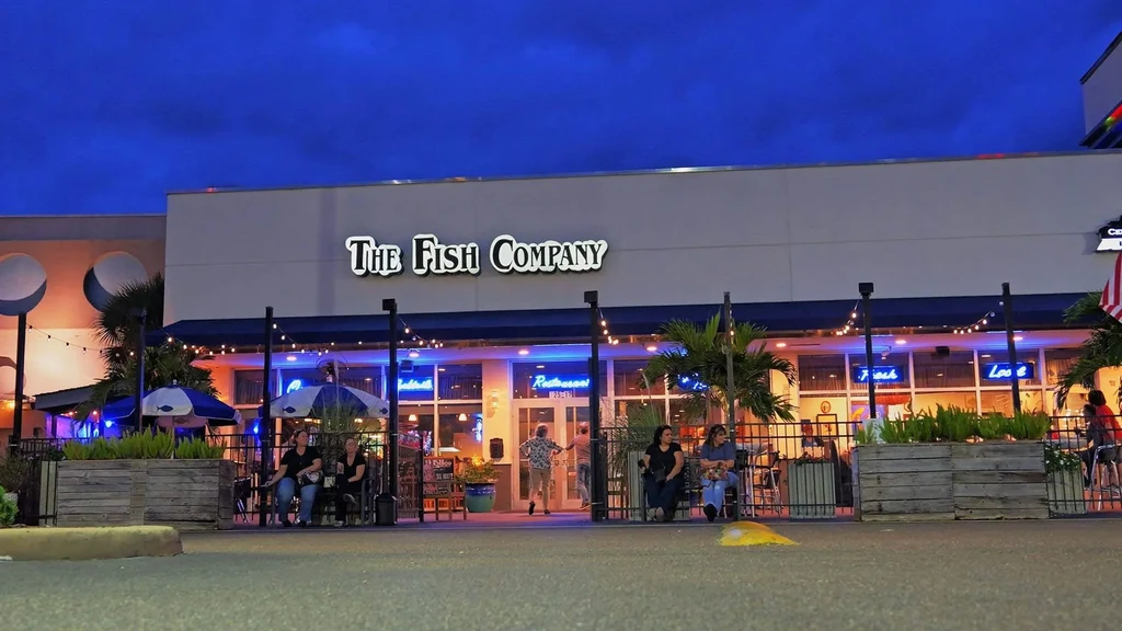Modern "The Fish Company" restaurant exterior illuminated at dusk with patio.