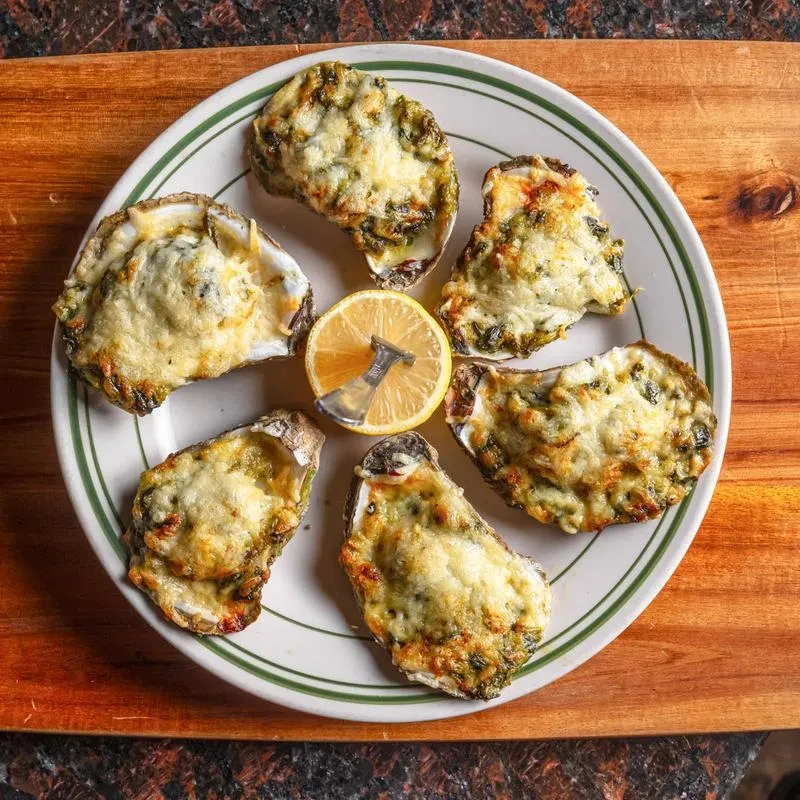Six baked oysters with cheese, herbs, and lemon on a striped plate.