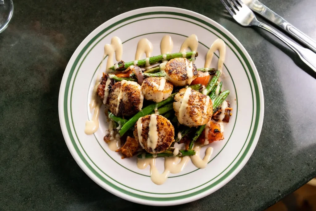 Seared scallops, green beans, sauce on white plate with green stripes.