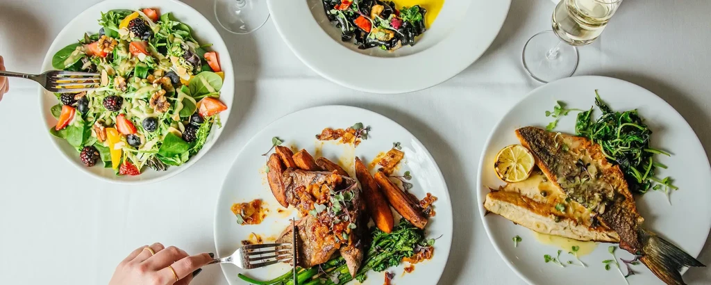 Overhead view: salad, meat, black pasta, and whole fish on a table.
