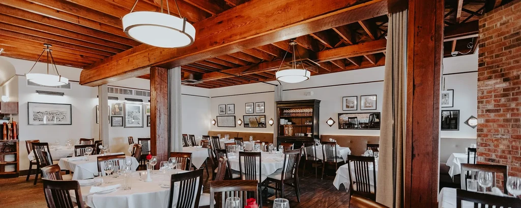 Elegant rustic-chic restaurant dining room with exposed beams and set tables.