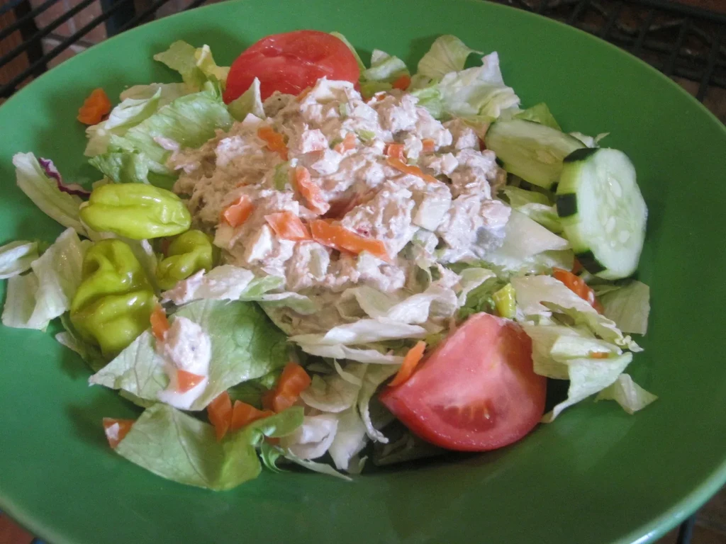 Tuna/chicken salad with lettuce, tomato, cucumber, carrots, pepperoncini in green bowl.