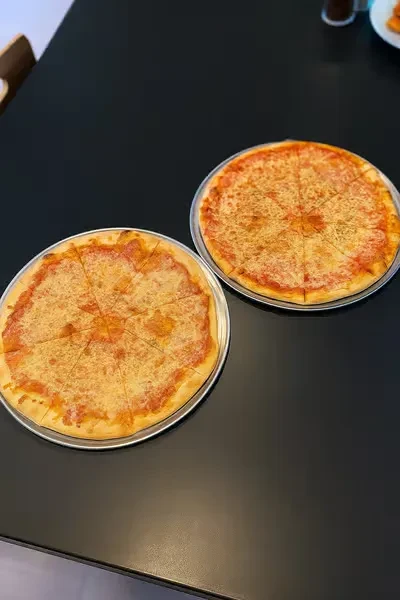 Two classic cheese pizzas, sliced, on metal pans.