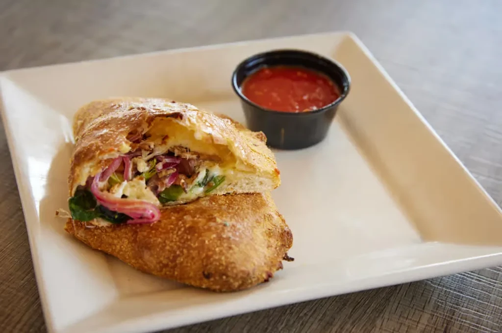 Calzone cut in half, showing cheese, vegetables, meat, and marinara.