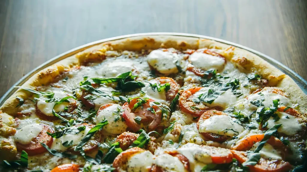 Golden-brown pizza with mozzarella, tomato slices, and fresh basil leaves.