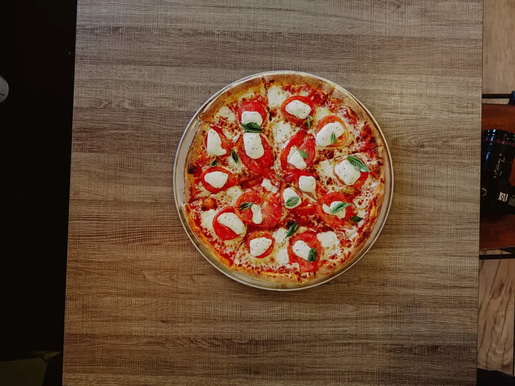 Freshly baked Margherita pizza with mozzarella, tomato, basil on wood.