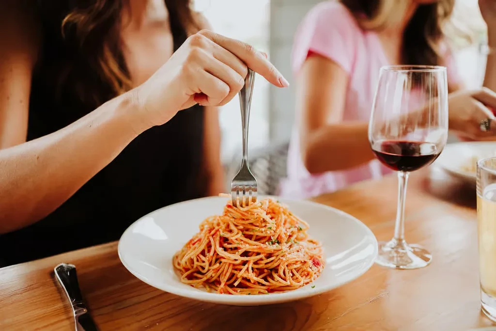 Close-up: Hand forking spaghetti with red sauce, cheese, and herbs.
