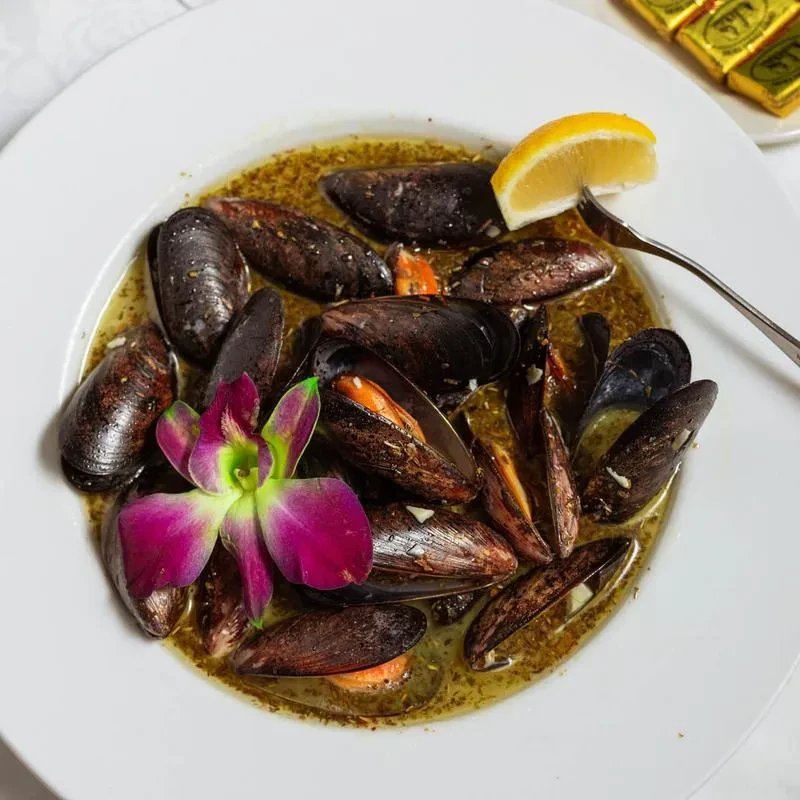 Close-up of steamed mussels in broth with lemon and orchid.
