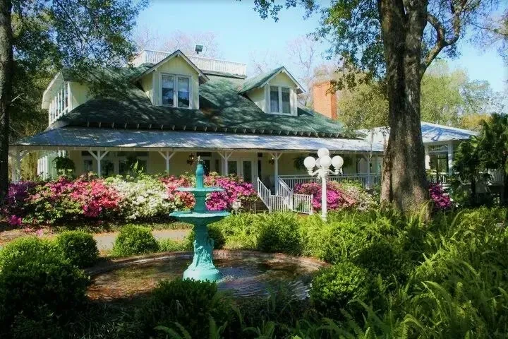 Yellow building with green roof, white veranda, fountain, and garden.