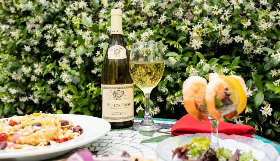 Outdoor meal: chilled white wine, pasta, shrimp, flowering bush.