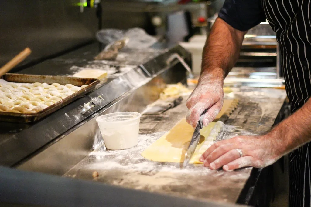 Chef's floured hands cut dough to make gnocchi in a kitchen.