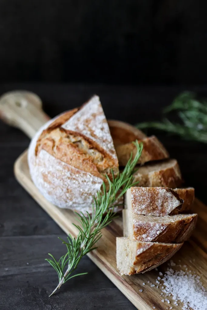 Sliced artisan bread with rosemary and sea salt on a wooden board.