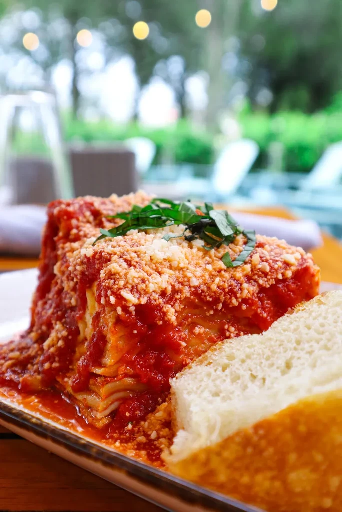 Generous lasagna slice with red sauce, parmesan, basil, and bread.
