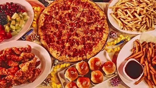 Festive table with pizza, fried chicken, fries, fruit, and sliders.