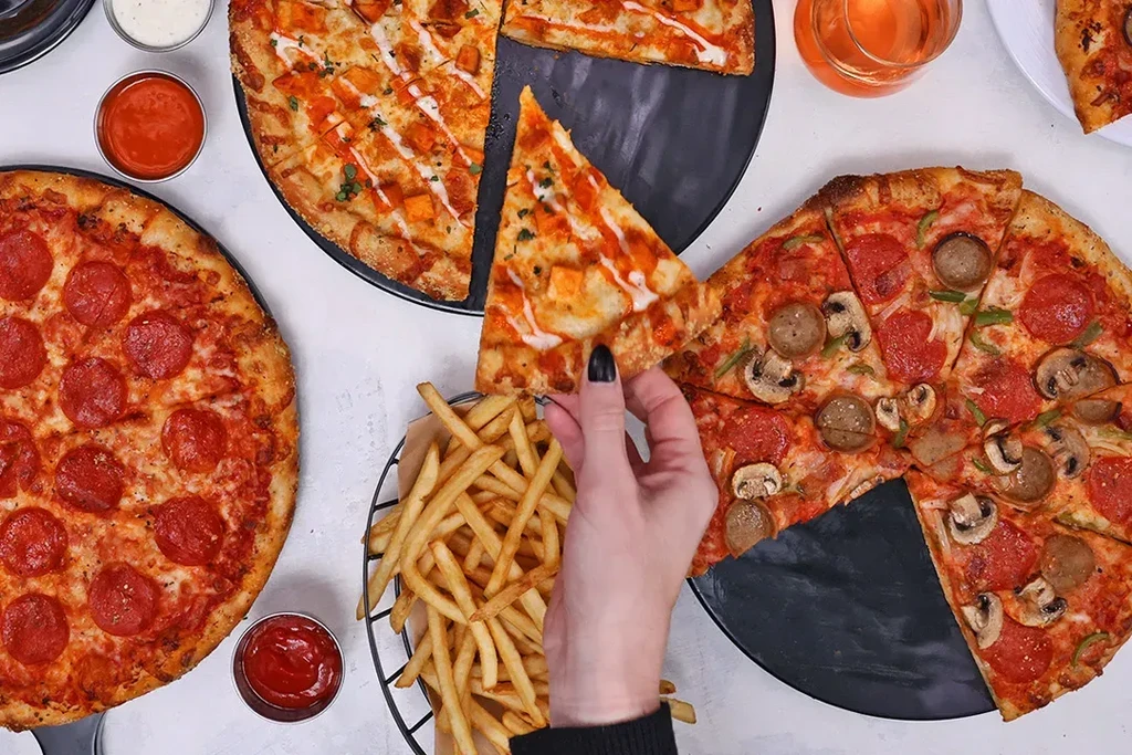 Hand lifting buffalo chicken pizza slice; pepperoni, supreme pizzas, fries.