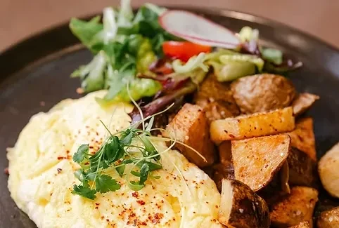 A plate of fluffy scrambled eggs, crispy roasted potatoes, and green salad.