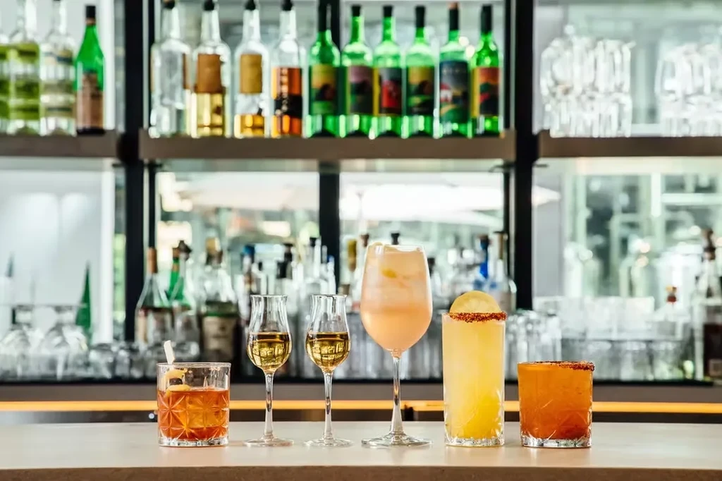 Five diverse alcoholic cocktails and spirits lined on a bar.