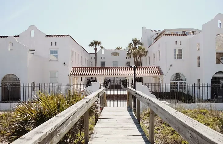 White Mediterranean resort, boardwalk, palm trees, under a sunny sky.