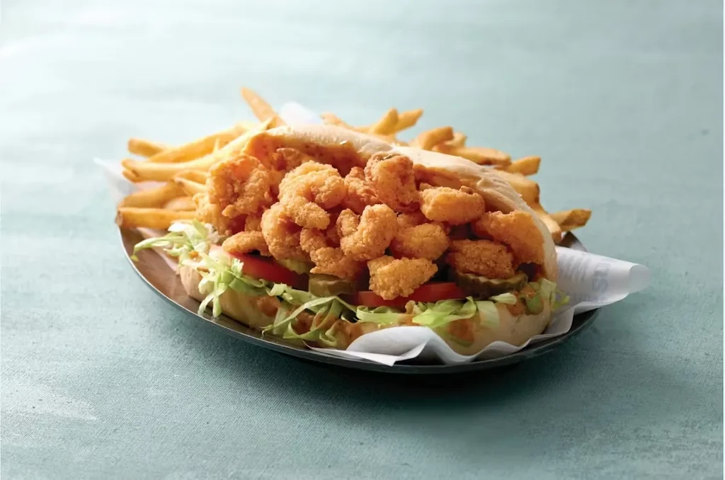 Golden-brown fried shrimp po'boy with lettuce, tomatoes, pickles, and fries.