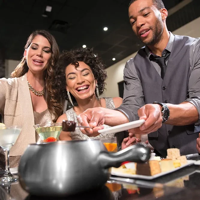 Man offers chocolate fondue to a laughing woman and friend.