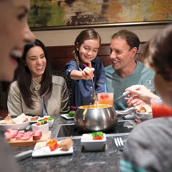 Smiling family dips food into cheese fondue at a restaurant.