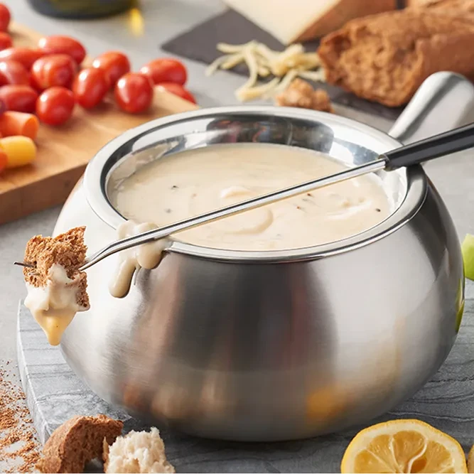 Stainless steel fondue pot, bread dripping melted cheese, with fresh sides.