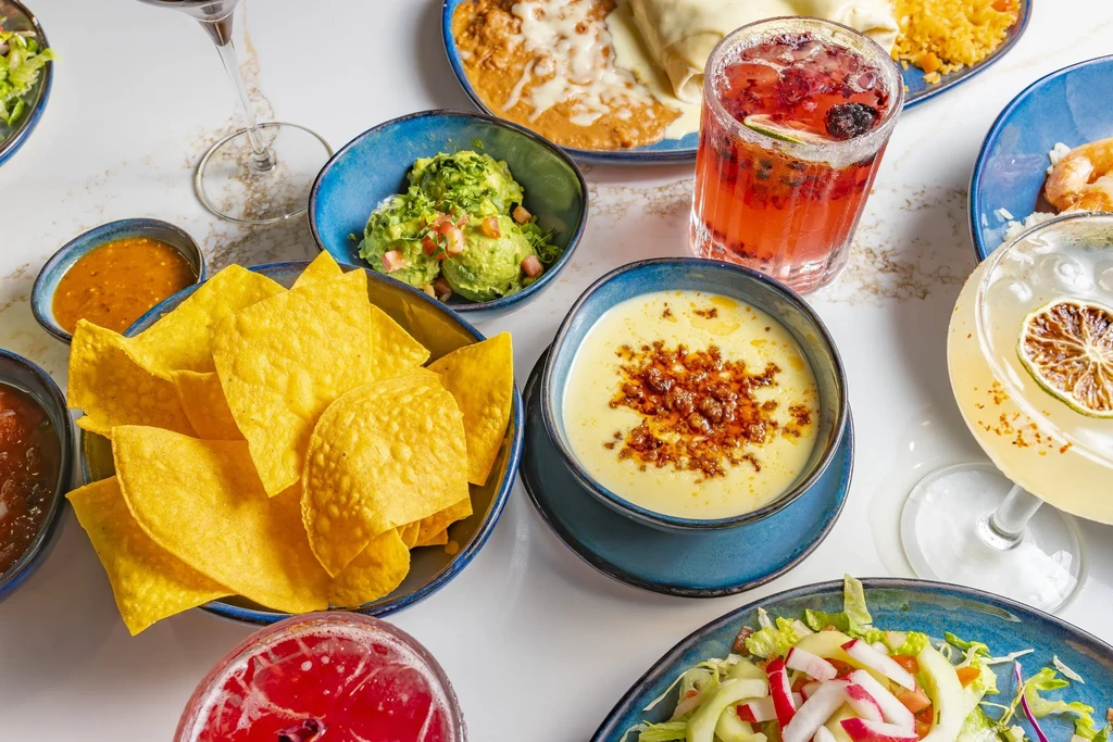Mexican restaurant table with chips, guacamole, queso, and various drinks.