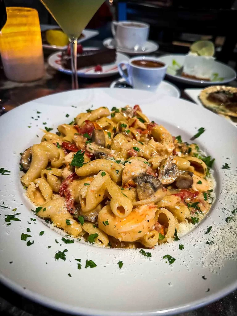 Close-up plate of creamy rigatoni with shrimp, mushrooms, tomatoes, and herbs.
