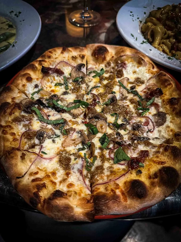 Gourmet pizza, sliced, with cheese, sausage, mushrooms, tomatoes, basil.