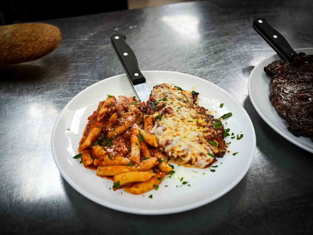 Two plates with penne pasta, chicken parmesan, and grilled steak.