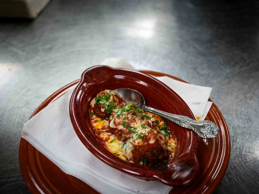 Meatballs baked in red sauce with melted cheese and green herbs.