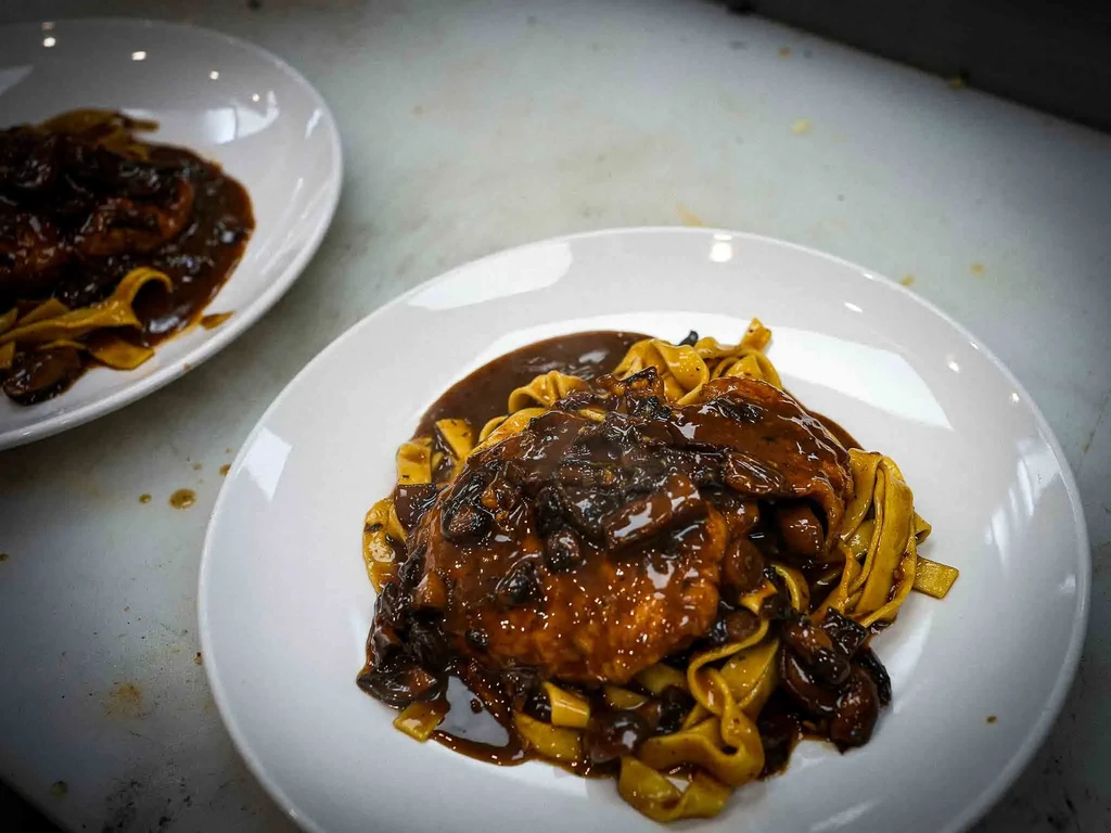 Two plates of pasta with protein and dark mushroom sauce.