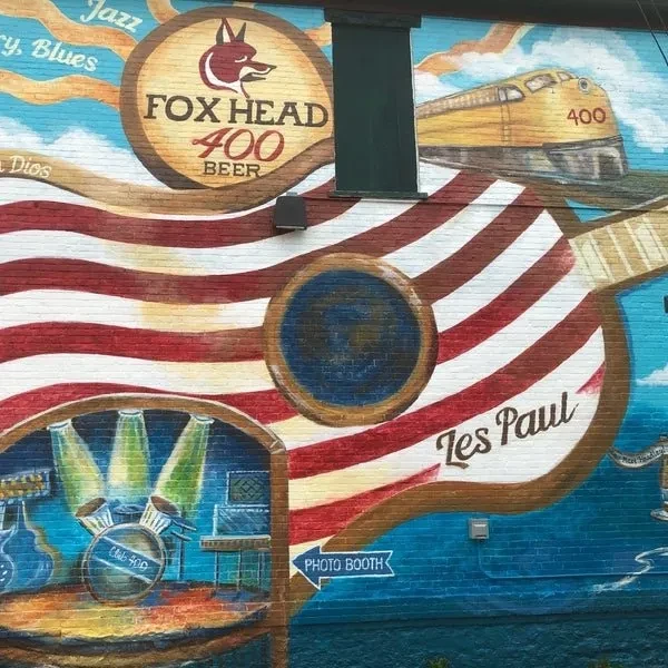 Vibrant outdoor mural on brick wall with music, trains, and local history.