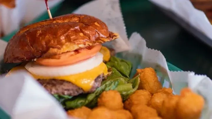 Cheeseburger with melted cheese, lettuce, tomato, onion in a green basket.