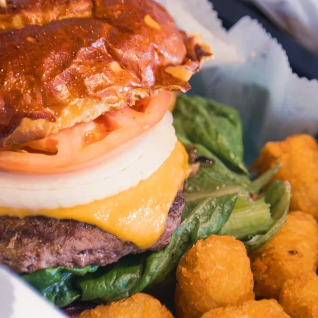 Close-up of a burger with melted cheese and a side of tater tots.