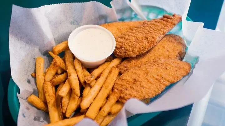 Three crispy fish fillets, thick fries, and dipping sauce in a basket.