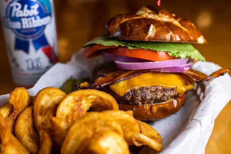Gourmet burger with curly fries and PBR beer in a basket.