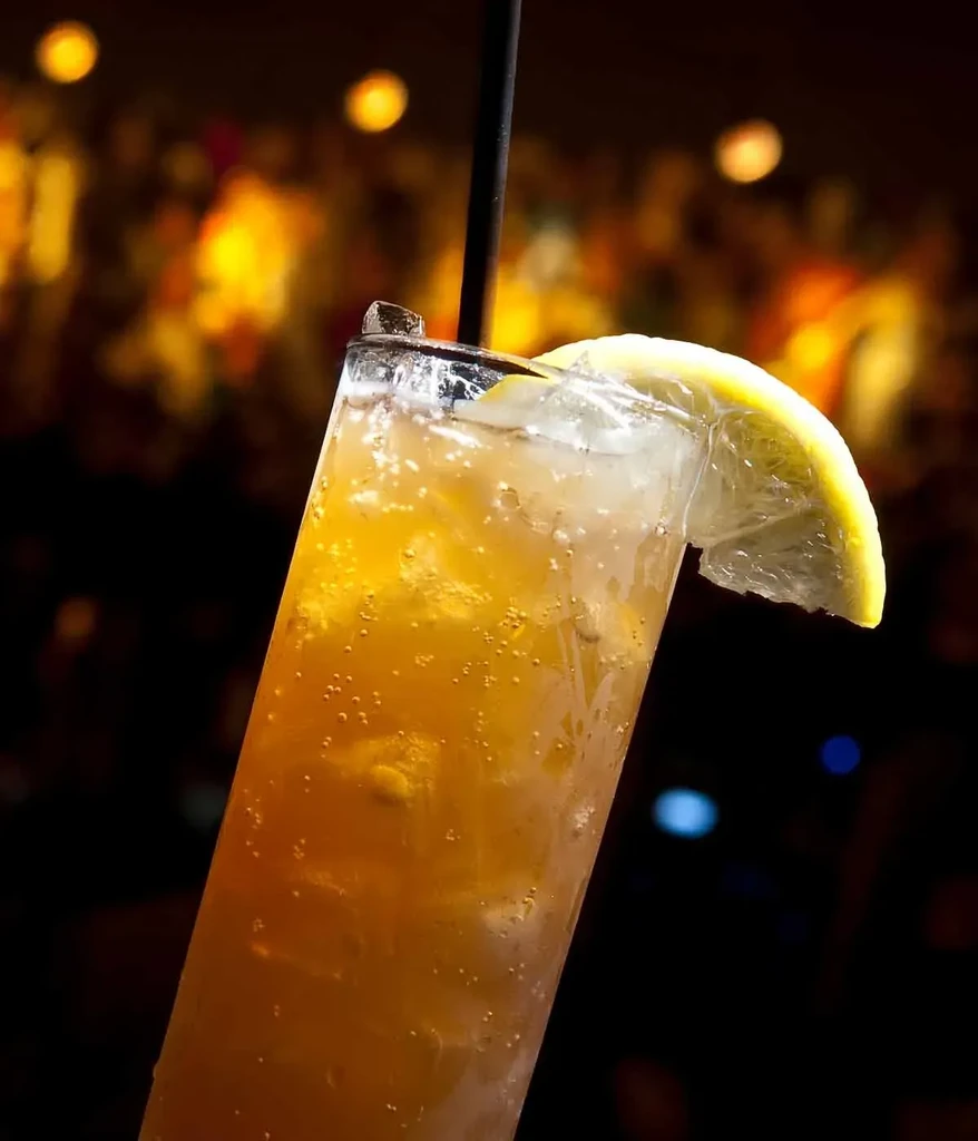 Amber carbonated drink with ice, lemon, and straw in a glass.
