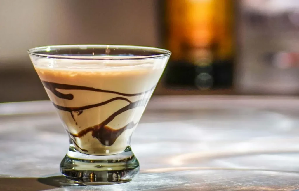 Creamy light-brown drink with chocolate syrup in a martini glass.