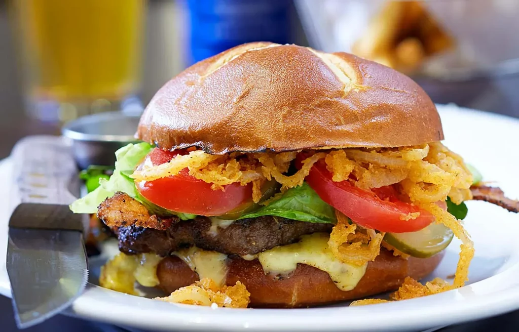 A large pretzel bun burger with melted cheese, bacon, and fried onions.