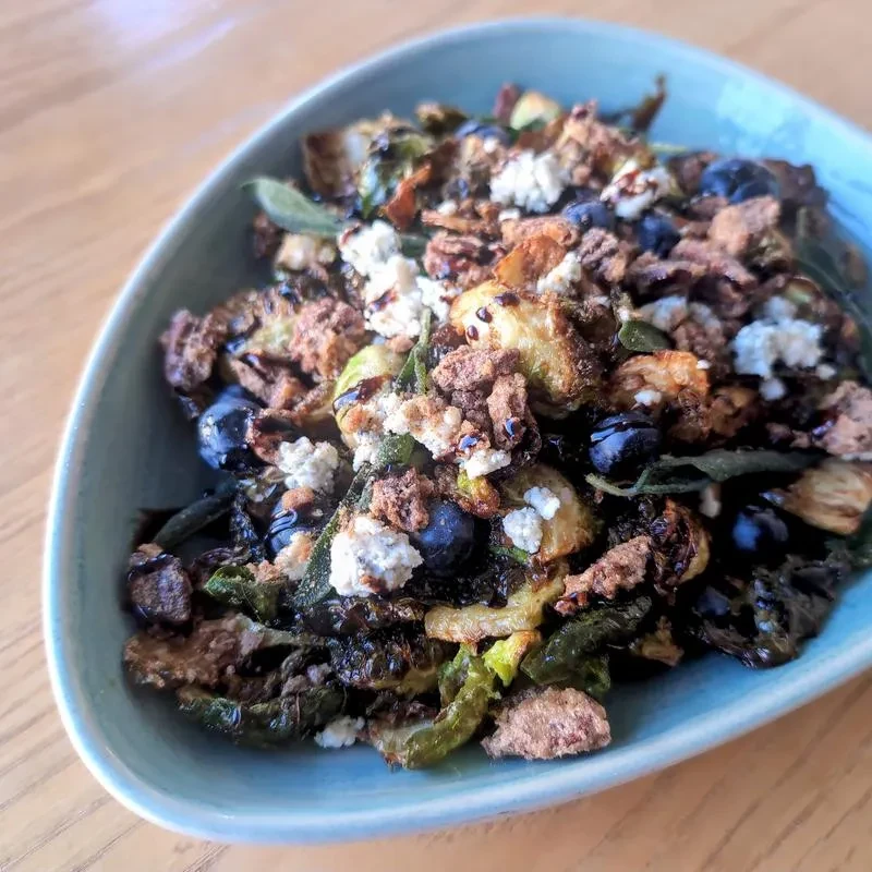 Overhead close-up of Brussels sprouts with blueberries, cheese, crumble, and glaze.