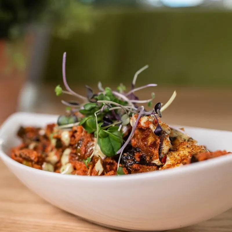 Boat-shaped bowl of reddish-orange food with microgreens and sauce.