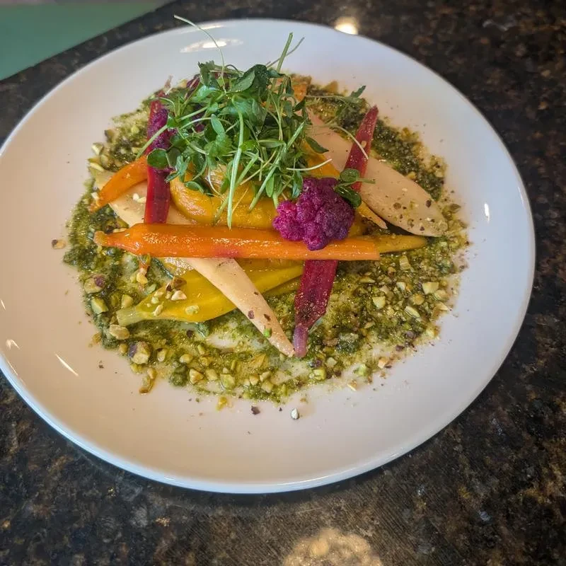 Meticulously plated roasted vegetables with pesto, microgreens, and pistachios.