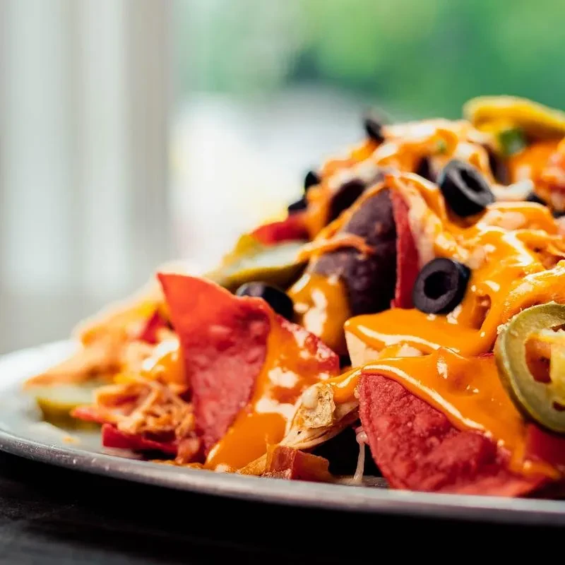 Generous plate of nachos with melted cheese, black olives, jalapeños, meat.