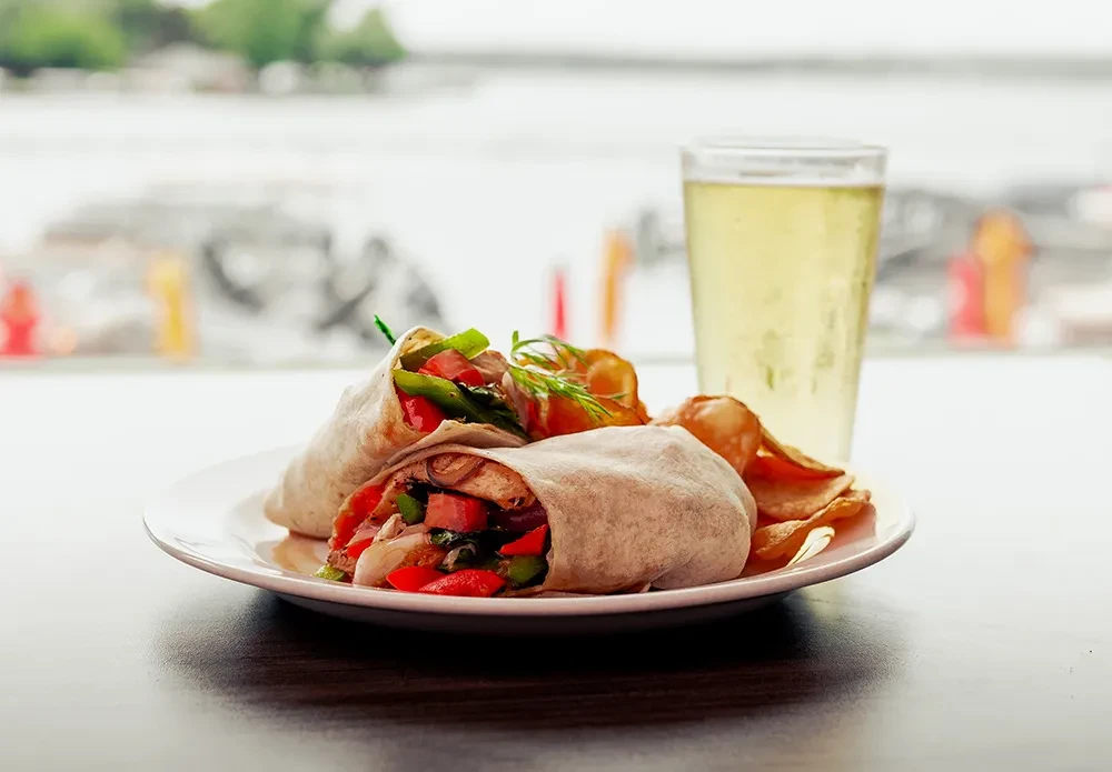 Two generously filled wraps, chips, drink, and waterside background.