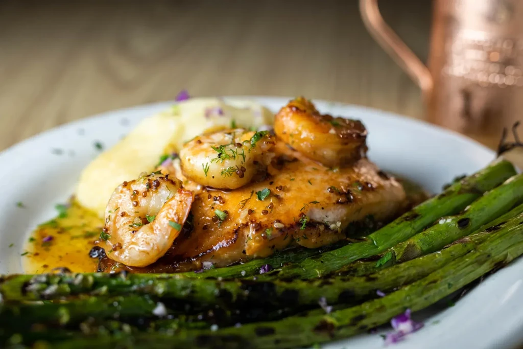 Plated seared fish with shrimp, mashed potatoes, and asparagus.