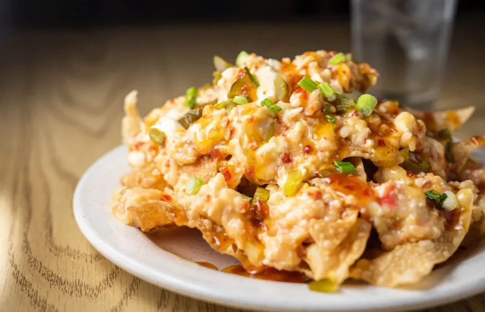 Plate of loaded nachos with creamy sauce, jalapeños, and green onions.