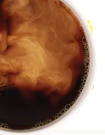 Swirling cream creates marbled patterns in dark coffee, in a white cup.